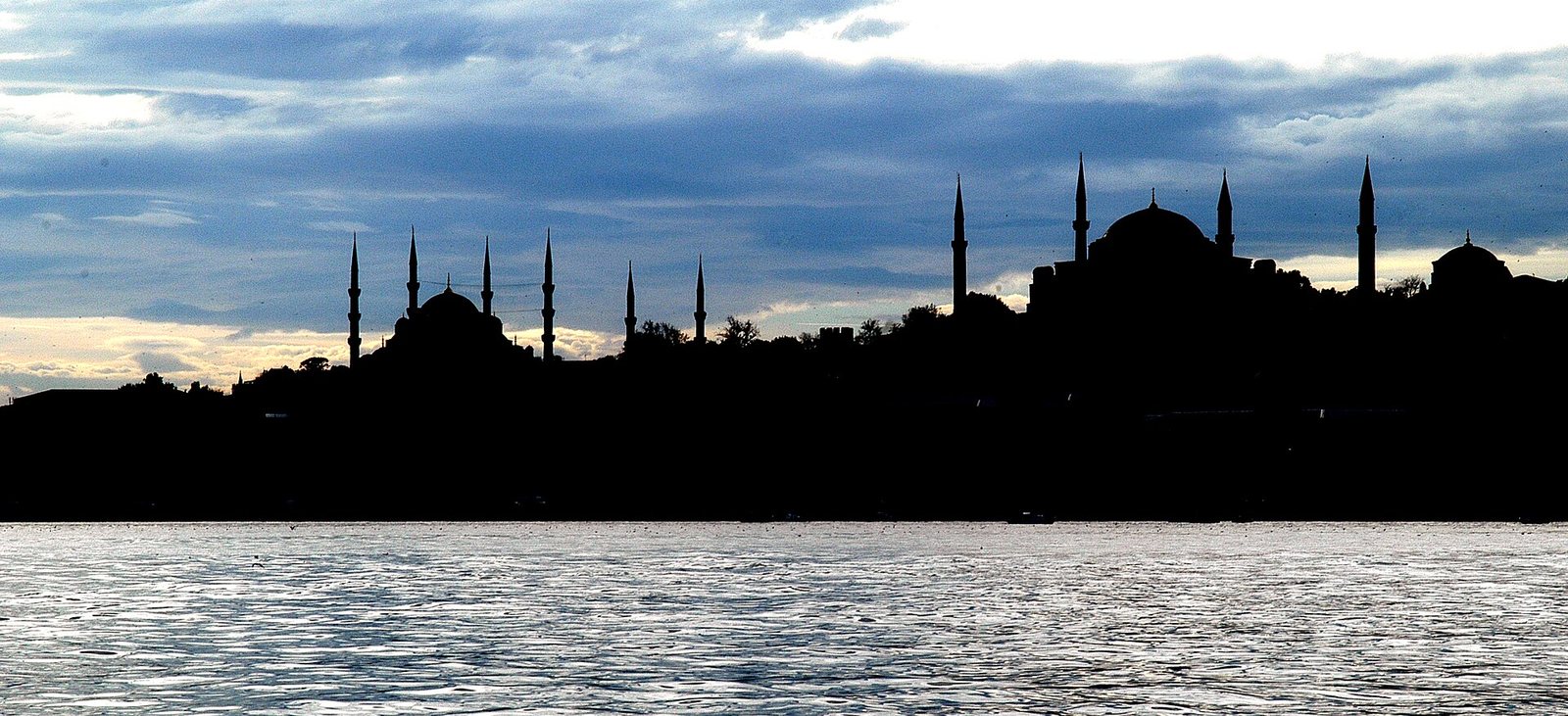 Historic Istanbul skyline silhouette at dusk — the domes and minarets of the Blue Mosque and Hagia Sophia over the water